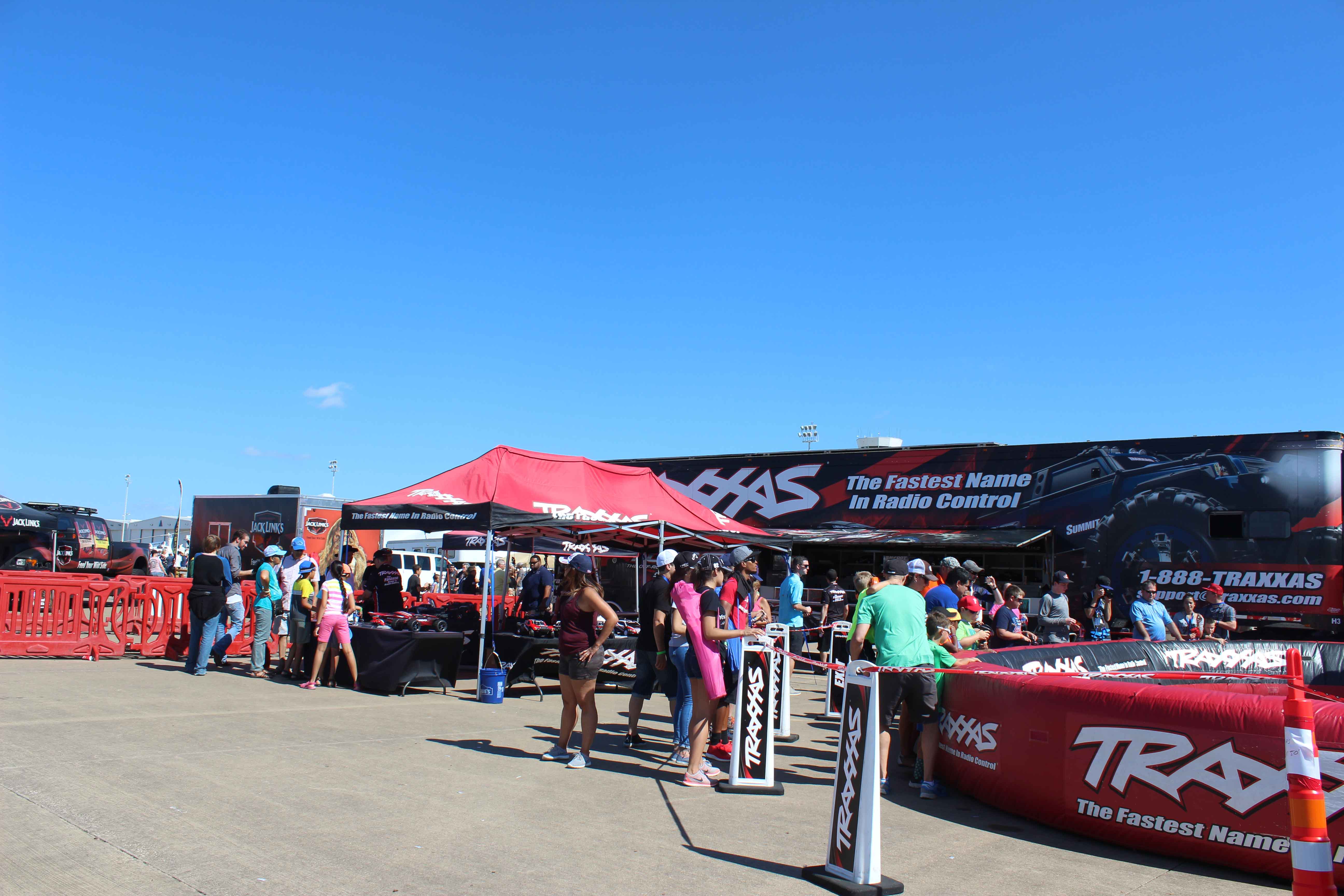 People enjoying a Traxxas radio control exhibit with a branded red tent in front of a branded semi trailer at an air show