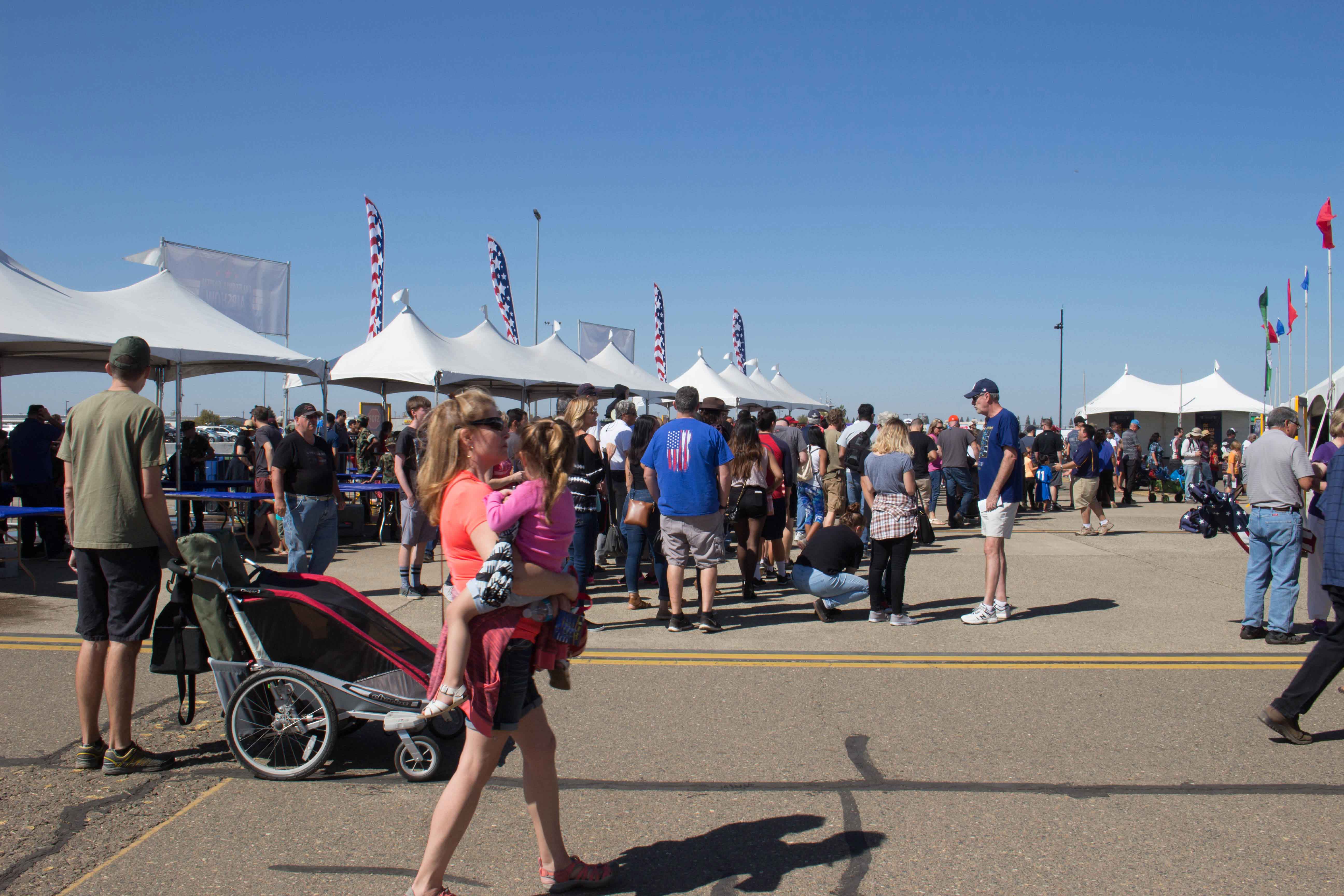 large crowd at air show entrance lined with large white tents and american flags