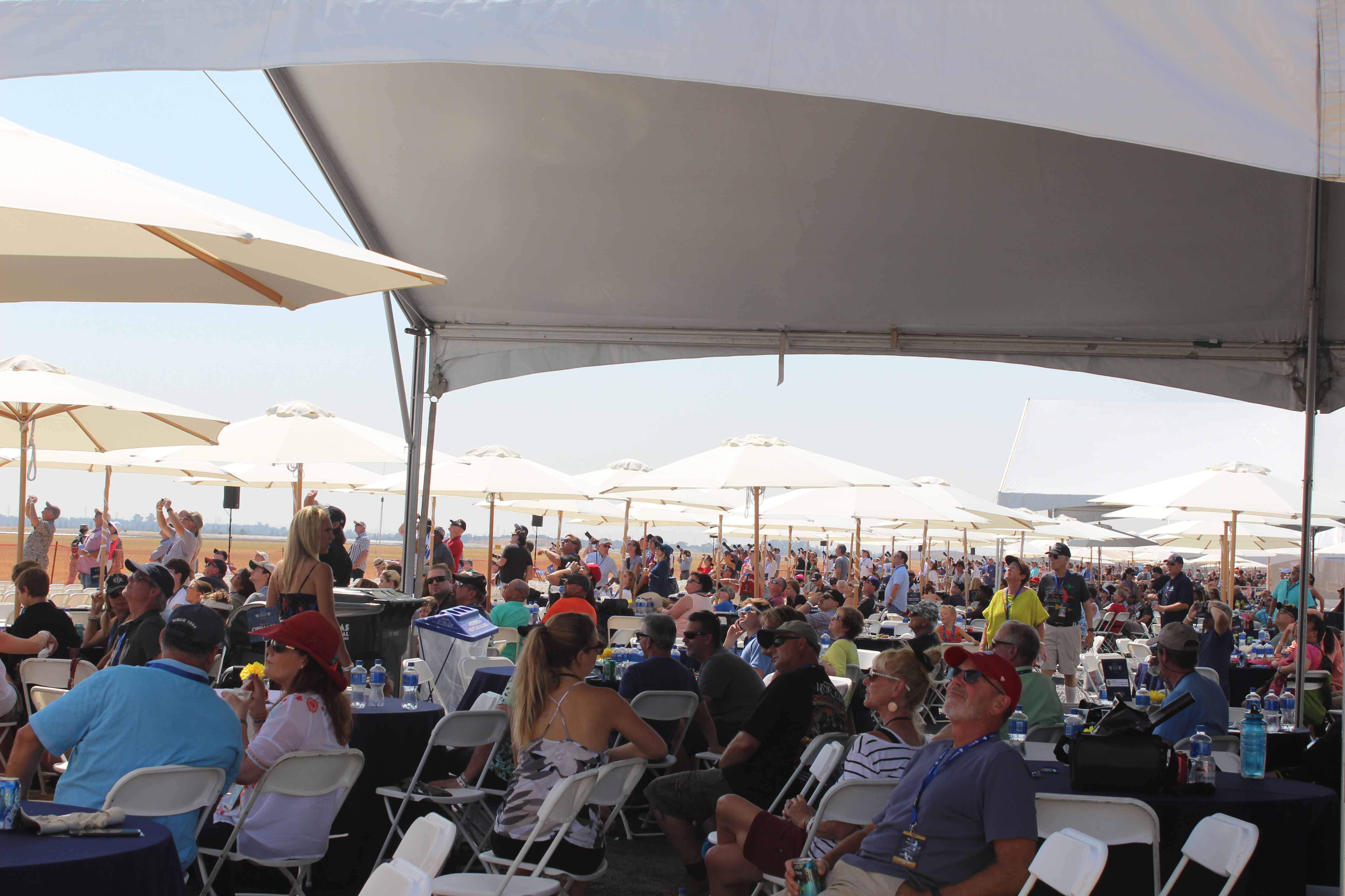 crowd sitting at tables under a large white tent at an air show chalet