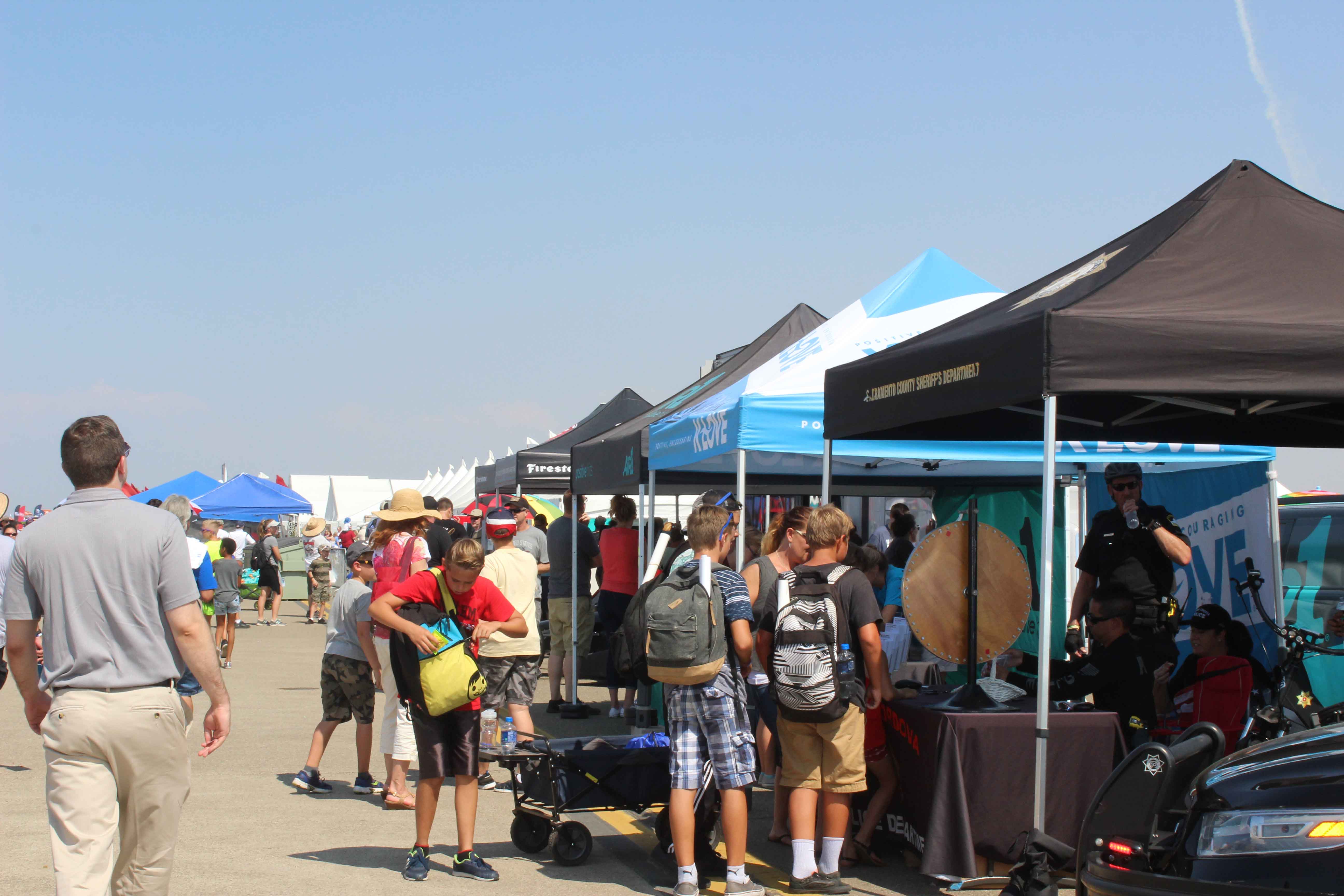 air show crowd visiting exhibits lined up next to each other at an air show on a clear day