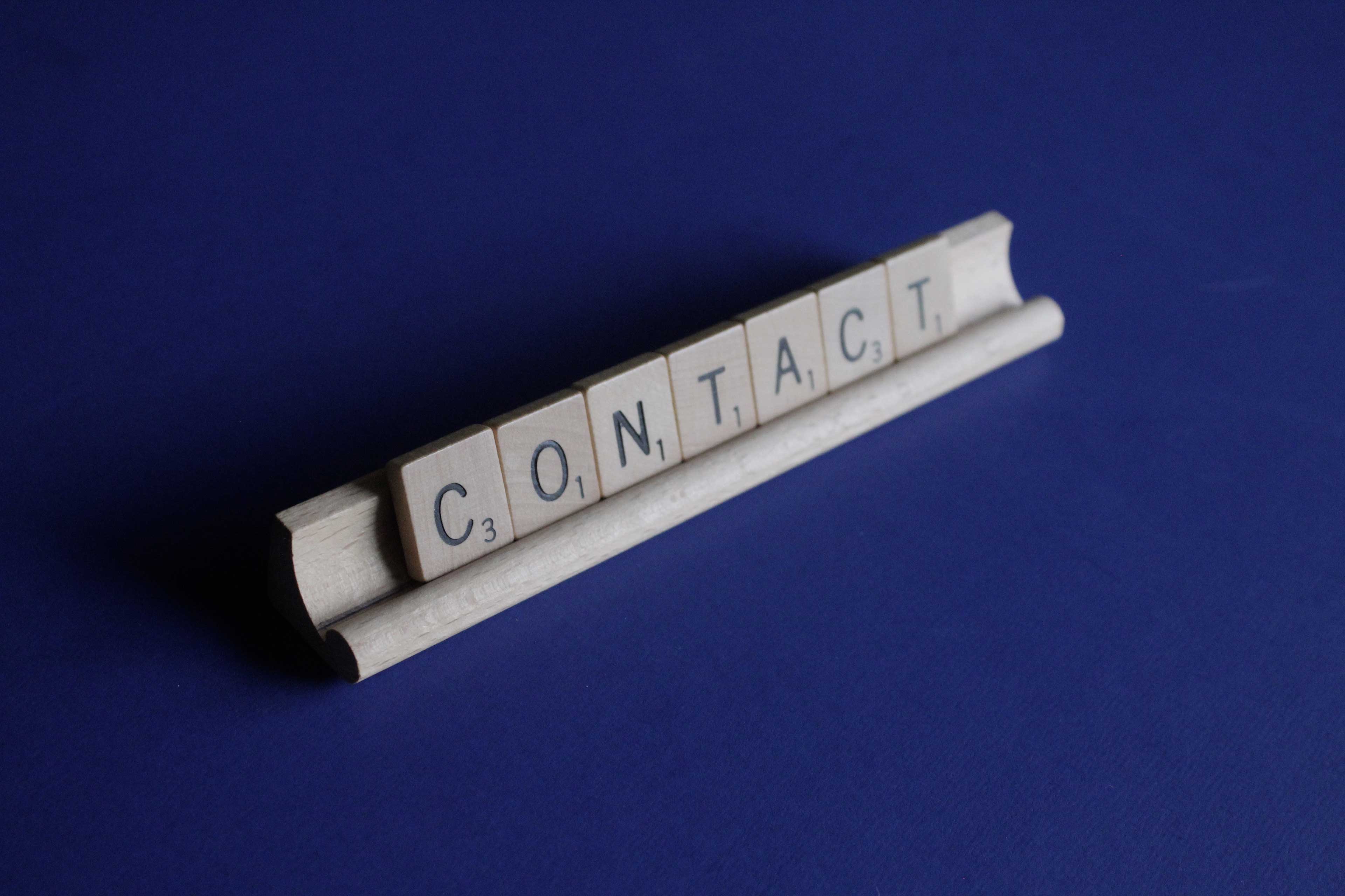 wooden scrabble letters spelling contact on a blue background