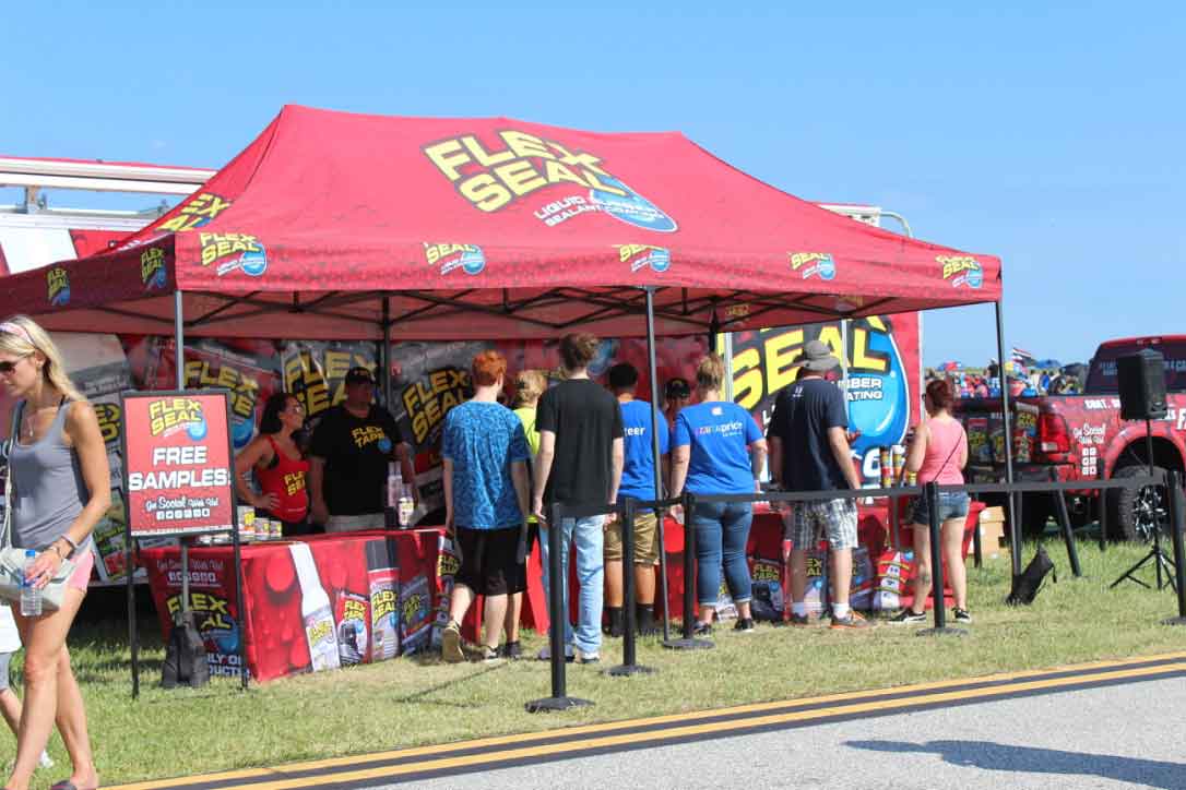 family visiting a Flex Seal exhibit under a large red branded tent at an air show on a clear day