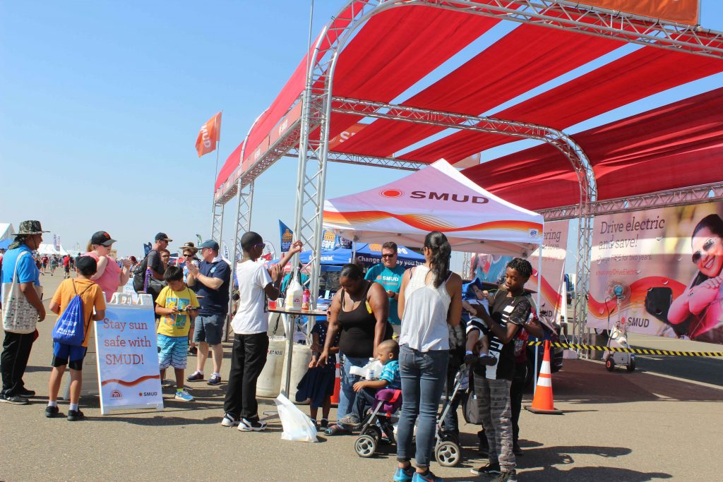 people under large SMUD branded tent visiting an exhibit at an air show