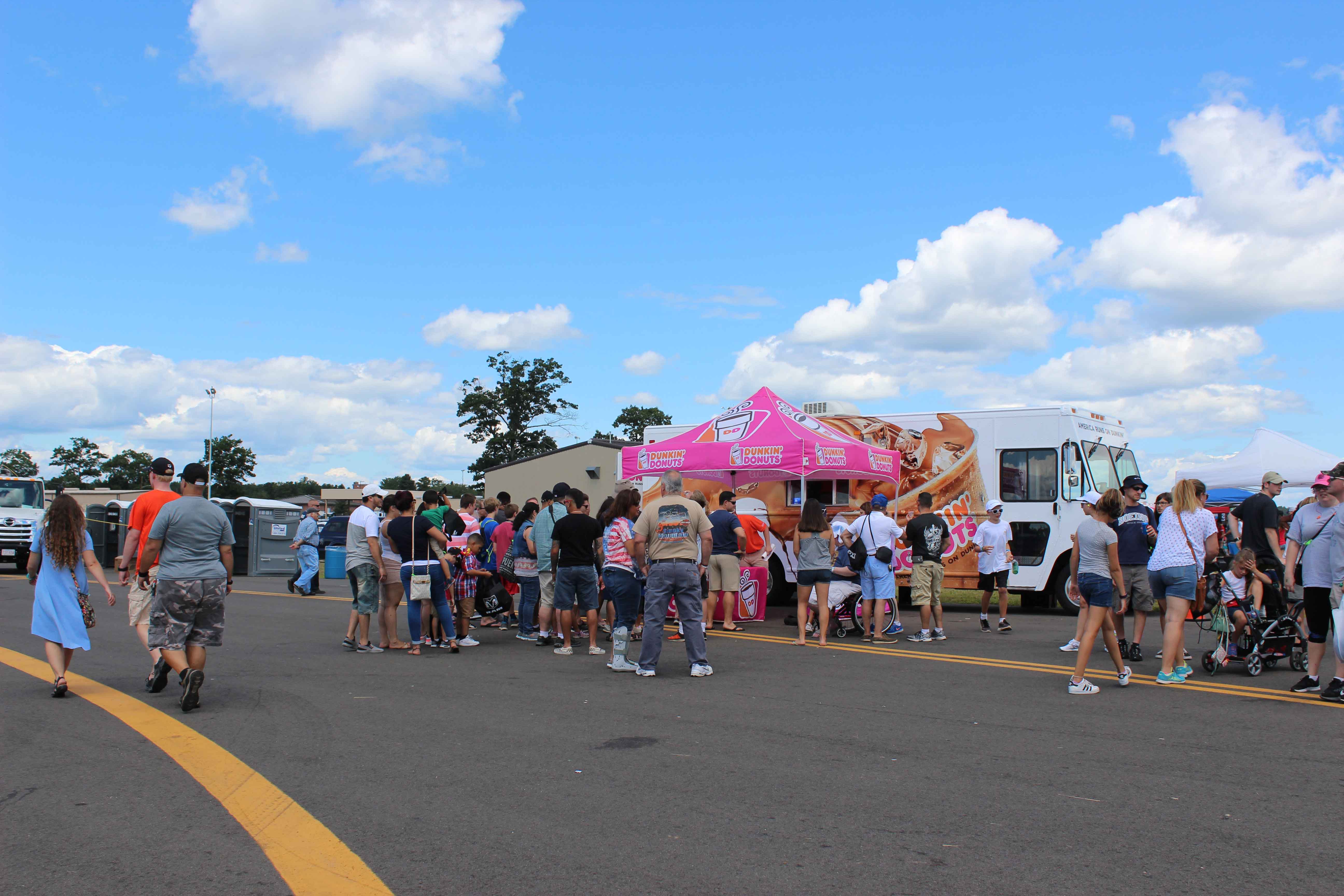 people in line to buy items from Dunkin Donuts food truck with a branded pink popup tent in front of it at an air show