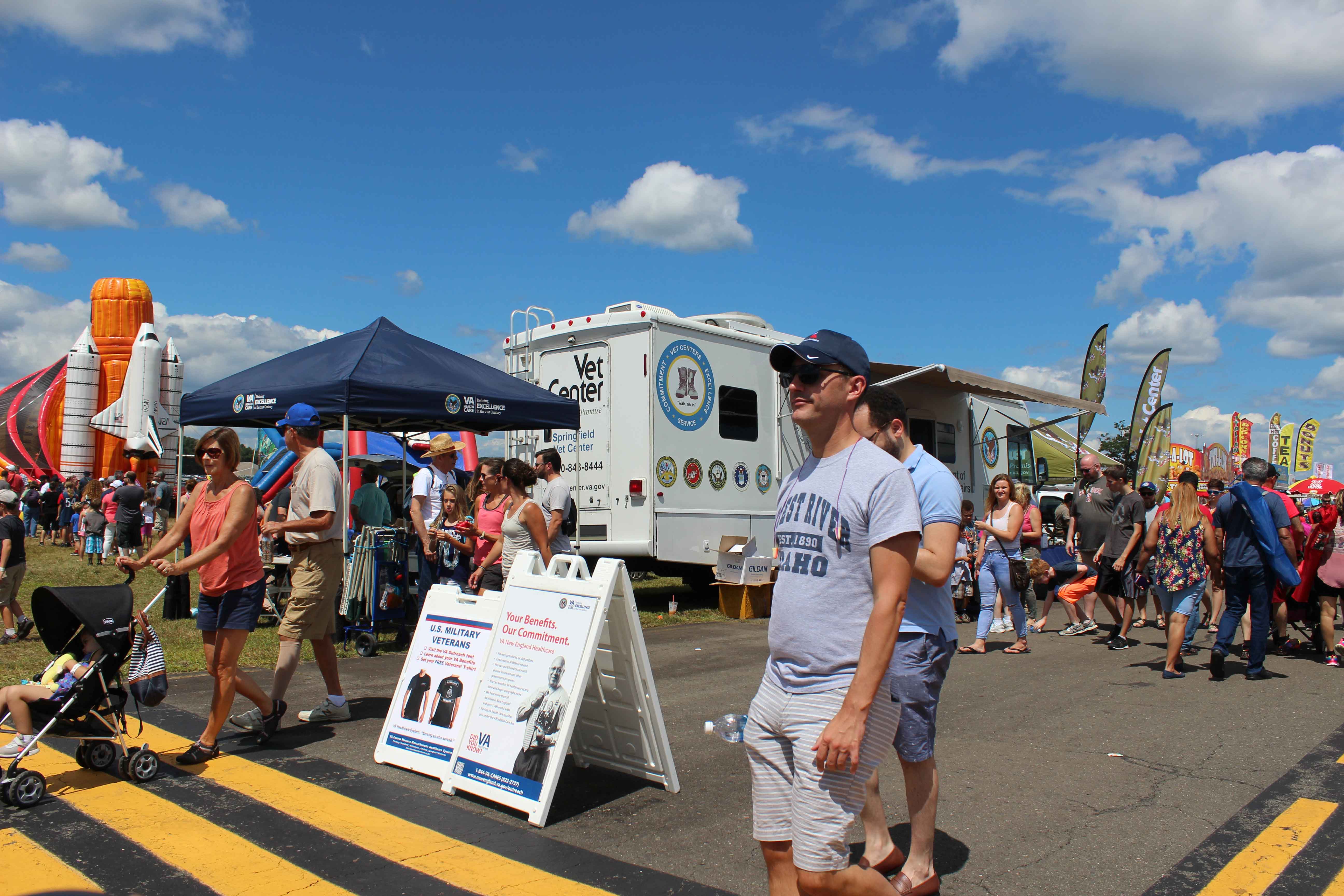 people walking past a Veteran's Affairs RV exhibit with a blue popup tent next to it at an air show