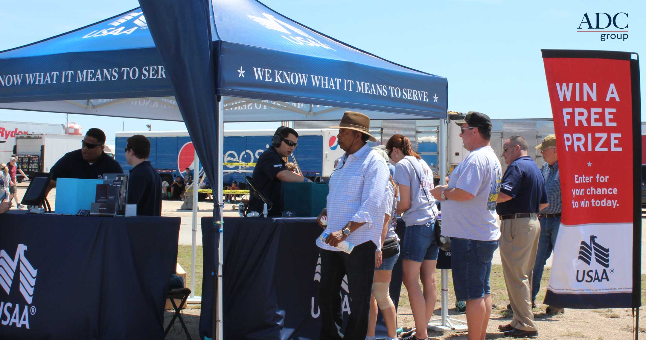 men and women visiting a USAA exhibit at an air show on a beautiful day